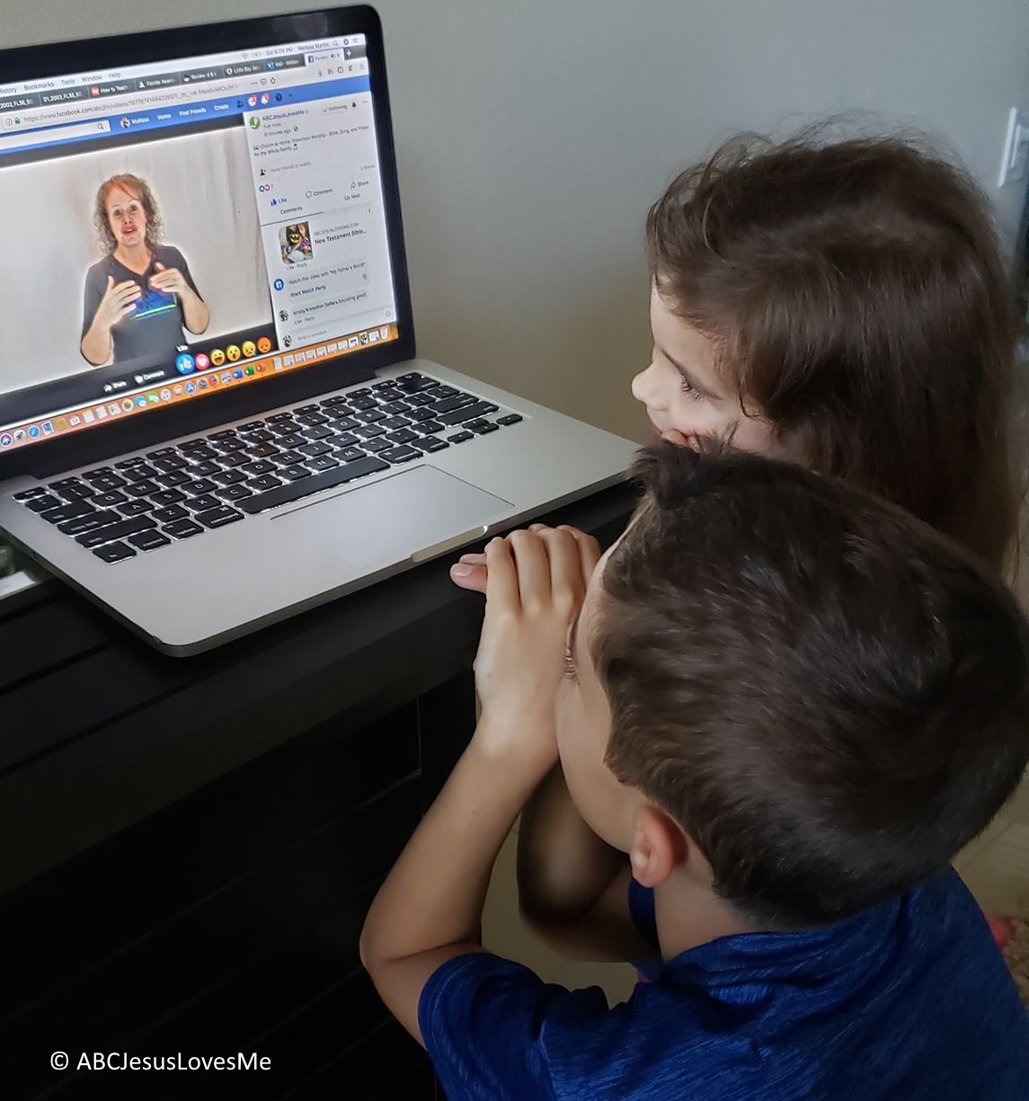 Two children watching Ms Heidi on a laptop